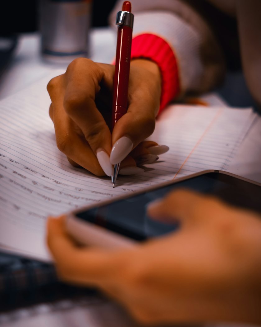 A person writing answers on paper beside a phone
