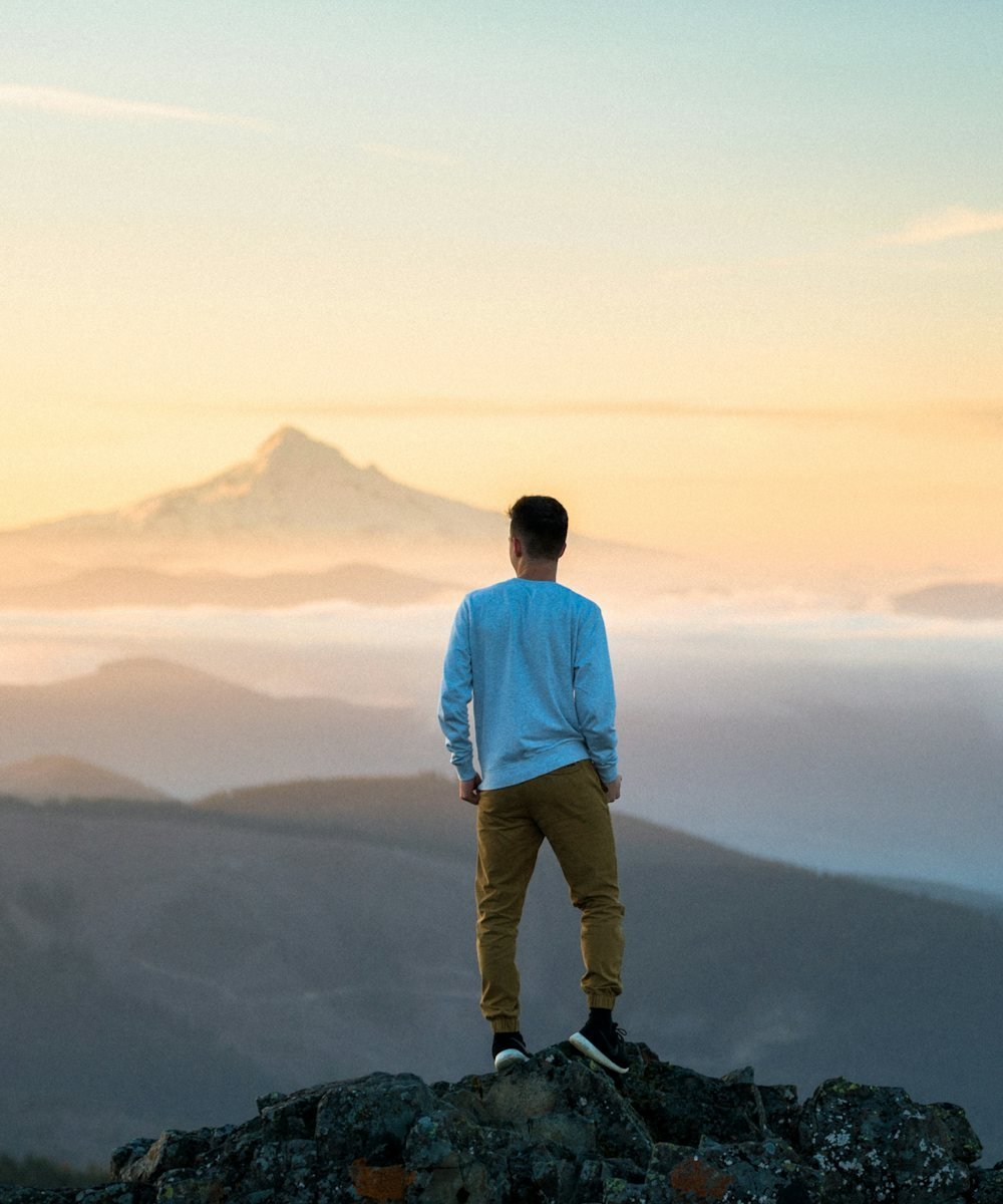 A young man standing on a hilltop at sunrise, looking out over the mountains