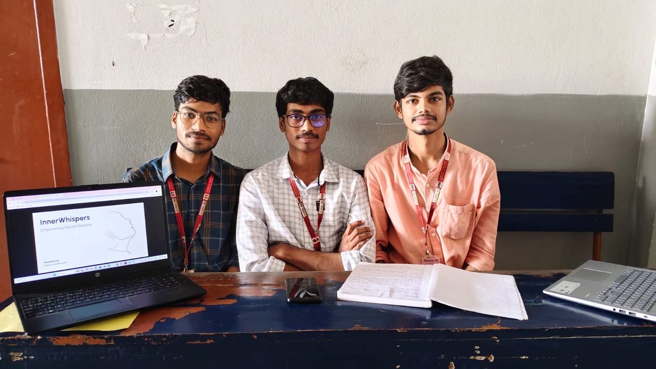Gopi, Bhanu and Dany seated at a desk, with a laptop showing the InnerWhispers pitch: Empowering Mental Wellness