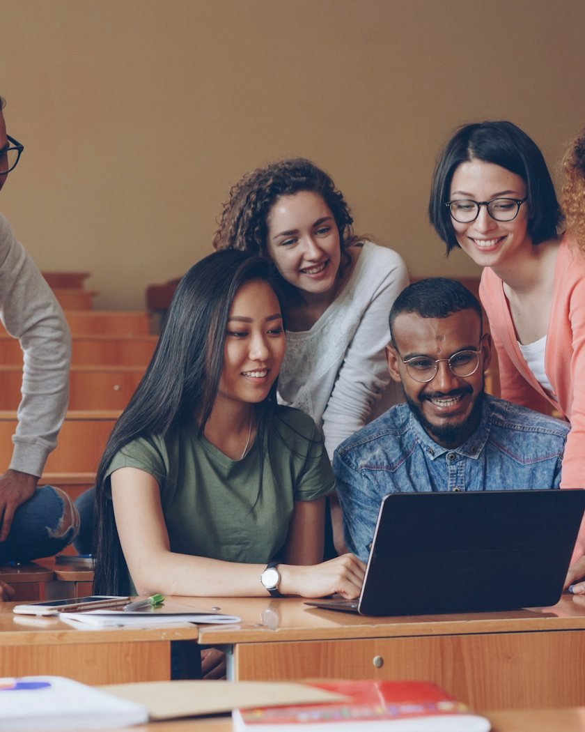 A group of smiling students working together around a laptop
