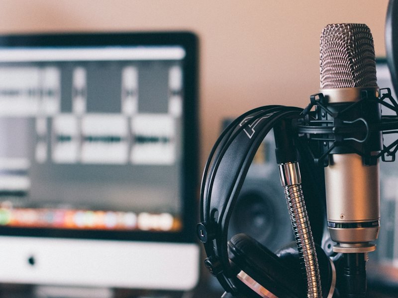 Headphones hanging on a studio microphone beside a computer
