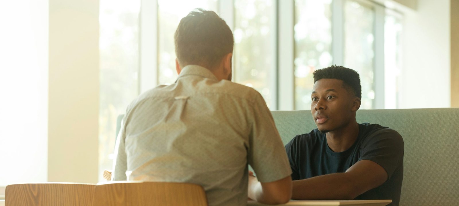 A young man talking openly with another man in a sunlit room