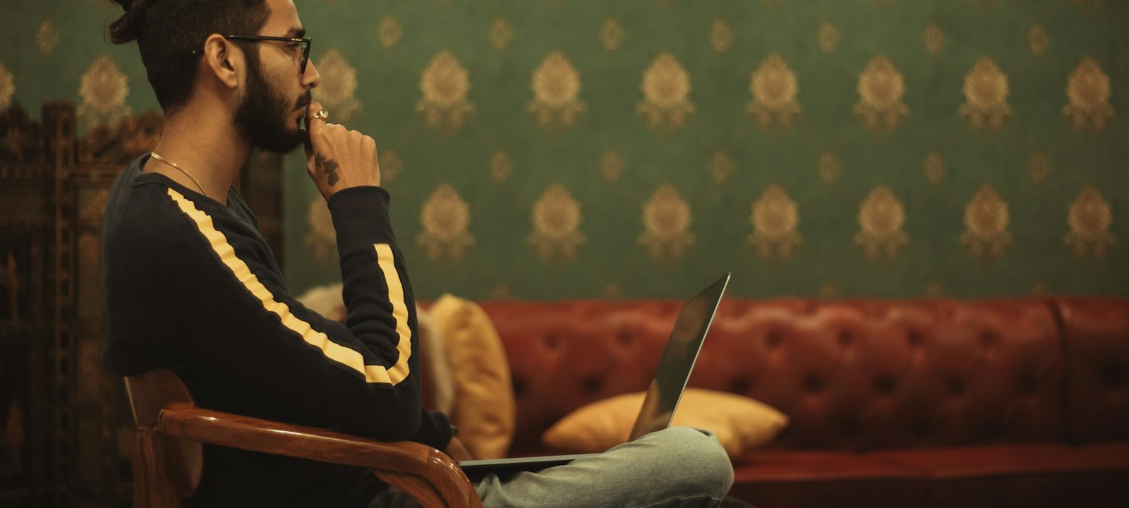 A young man sitting in a chair with his laptop, lost in thought