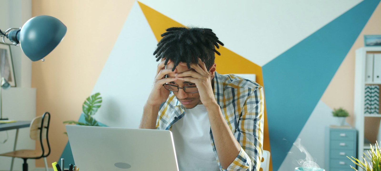 A man at his desk with his head in his hands in front of a laptop
