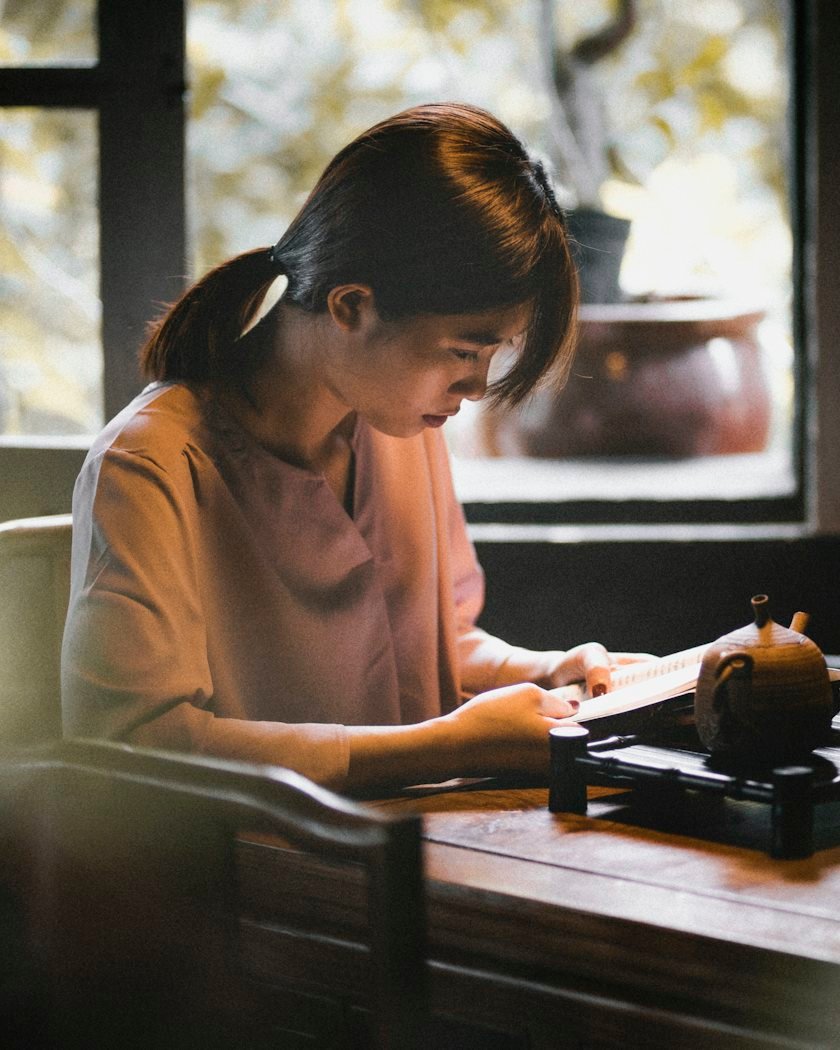 A young woman writing in a notebook at a sunlit table