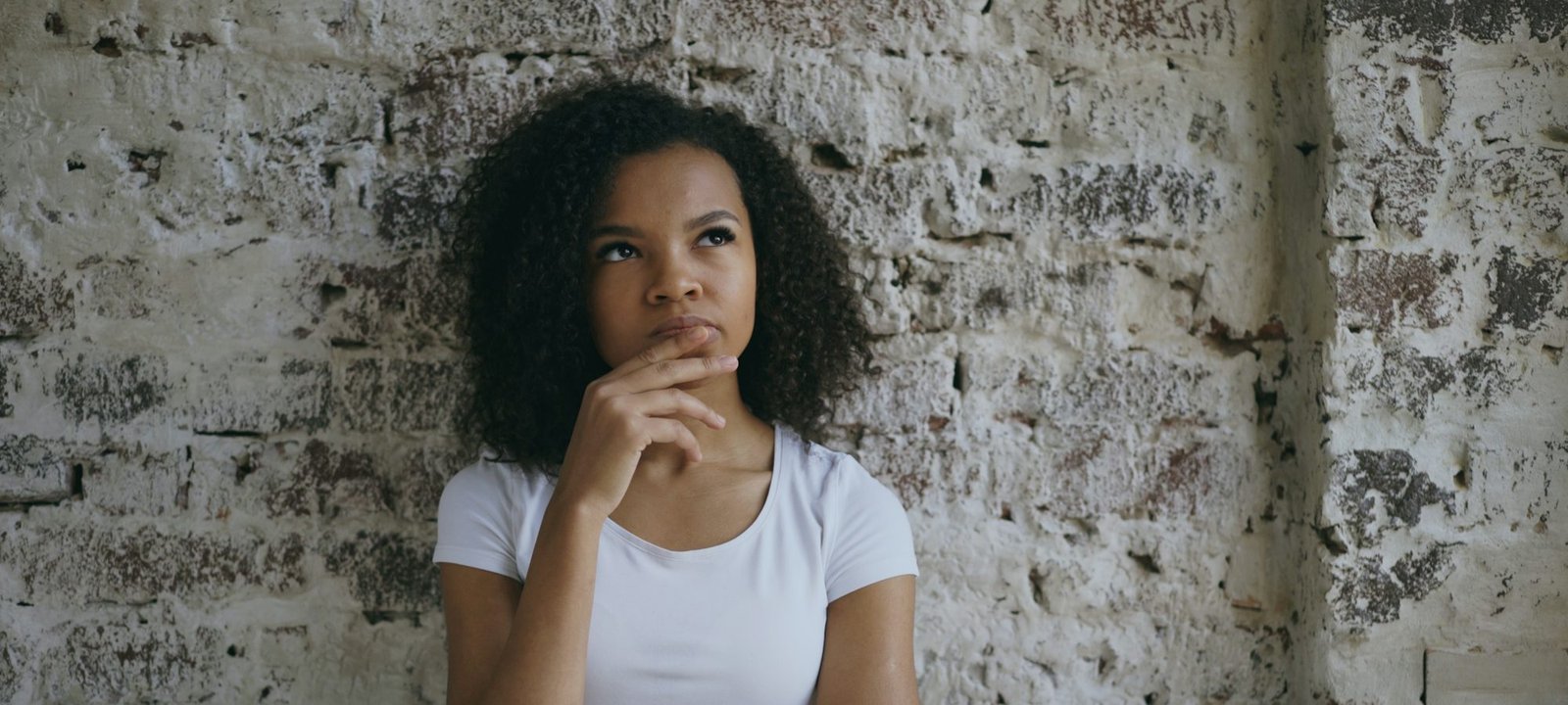 A young woman leaning against a wall, thinking