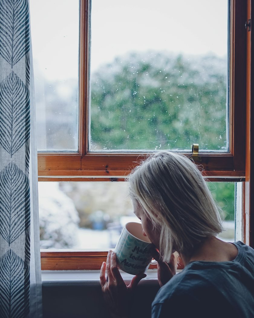A woman sipping a warm drink by a rainy window
