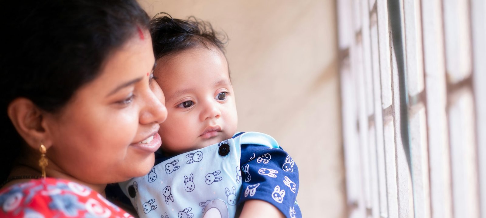 A mother holding her baby close by a window